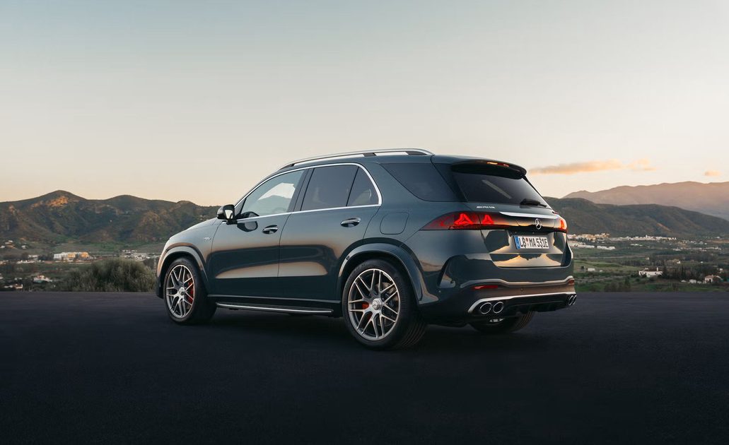 rear three quarter view, dark suv parked on mountain overlook at sunset, valley town and hills in background.