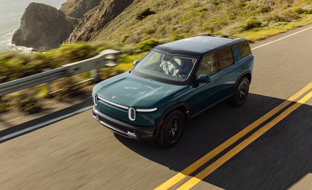 front three quarter view of green suv driving on coastal highway beside ocean cliffs.